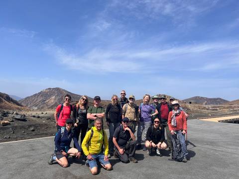       Hiking group poses on a volcanic plateau surrounded by barren peaks under clear blue sky.
  