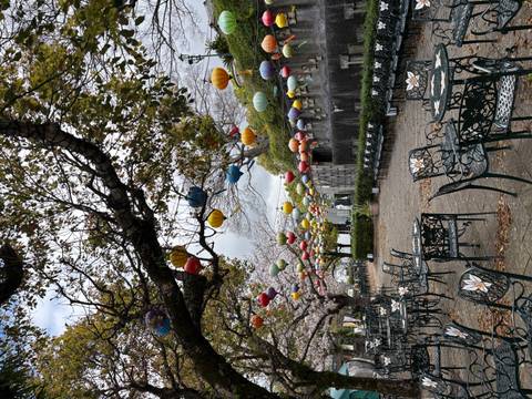       Outdoor café garden adorned with colorful hanging lanterns beneath blooming cherry trees.
  