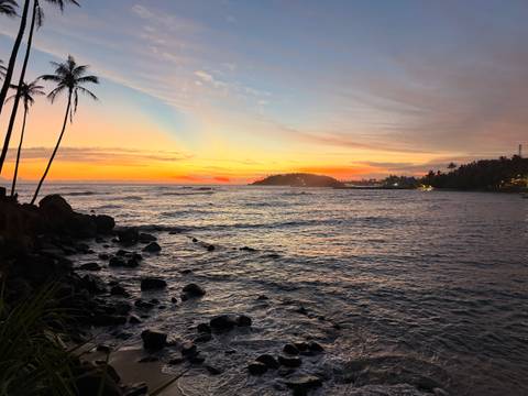       Vibrant twilight sky glows over a rocky coastline and distant headland in Sri Lanka.
  