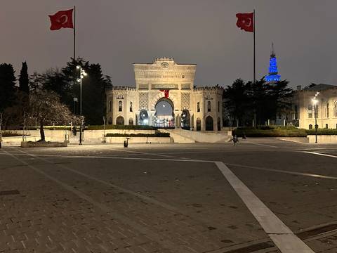       Evening view of Istanbul University’s historic gate illuminated against the night sky.
  