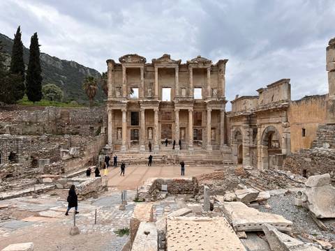       Ruins of the Library of Celsus in Ephesus with scattered visitors exploring the ancient site.
  