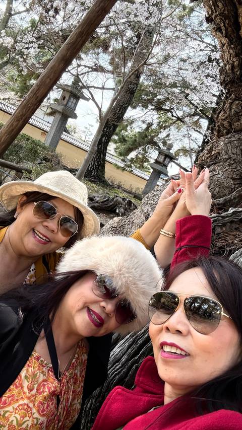       Close-up selfie of three travellers partly cropped while raising hands beside a gnarled tree.
  