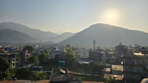       Morning sun over Pokhara’s rooftops and surrounding verdant hills with light mist.
  