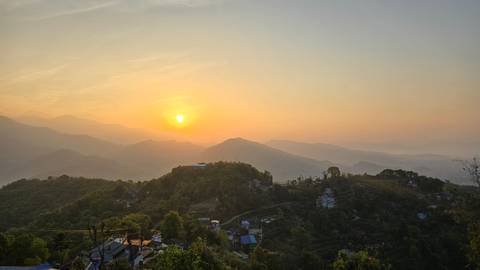       Soft orange sunrise lighting Himalayan foothills and small village houses below.
  