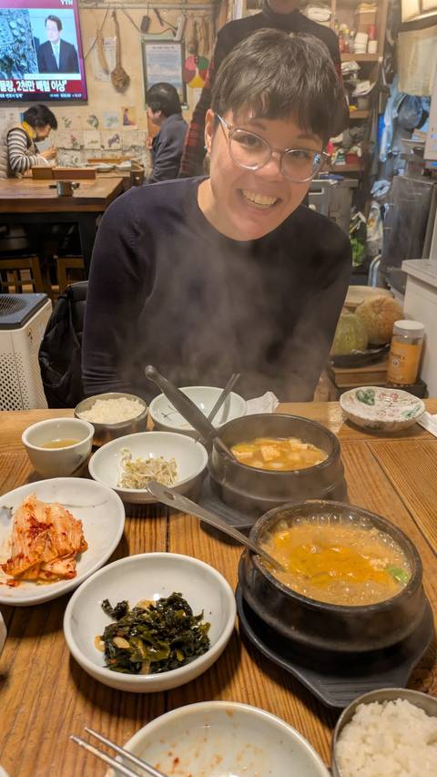       Table of steaming Korean dishes including soup, rice and side plates inside a casual restaurant.
  