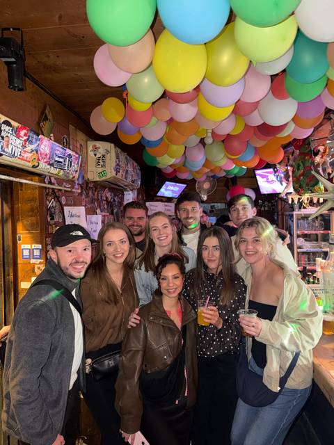      Friends gathered inside a lively bar decorated with colorful balloons.
  