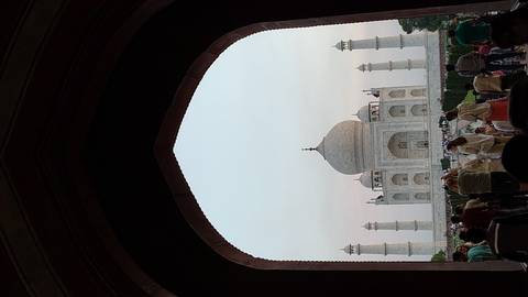       Taj Mahal framed by a dark arched gateway at dusk with visitors gathered in the foreground.
  