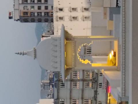       Small illuminated dome pavilion on a rooftop at dusk with cityscape in soft focus.
  