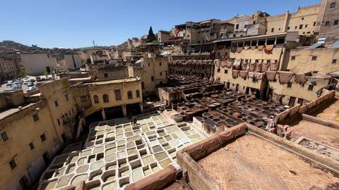       High view of Fes tannery with vats of dye and surrounding old city buildings.
  
