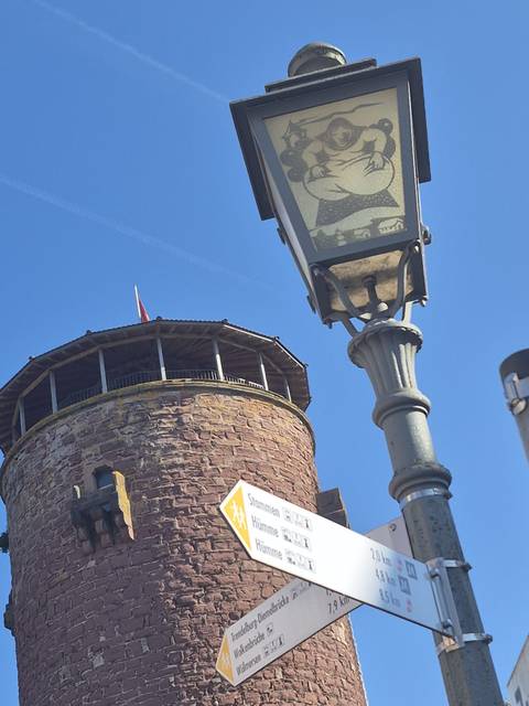       Close-up upward view of a round stone tower and an old streetlamp against a clear blue sky.
  