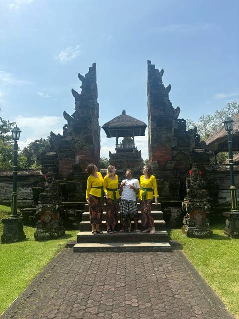       Travellers wearing yellow temple sashes pose playfully between ornate stone gate pillars in Bali.
  