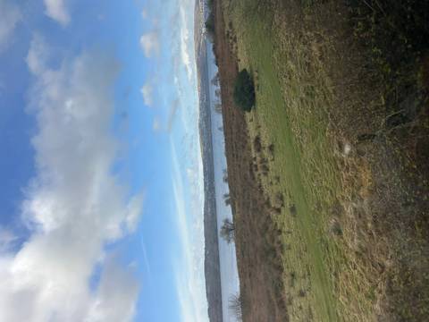       View of a loch and distant hills under scattered clouds captured through a vehicle window.
  
