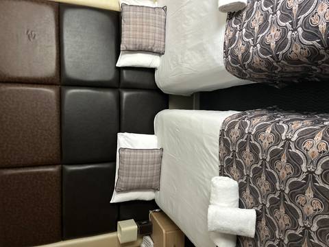       Simple twin hotel beds with patterned runners and plaid cushions in a compact room.
  