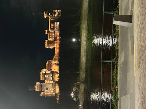       An illuminated riverside castle reflects shimmering light onto the water during the night.
  