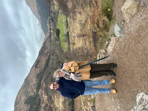       A couple poses at a viewpoint overlooking the iconic Glenfinnan Viaduct amid rugged Highlands scenery.
  