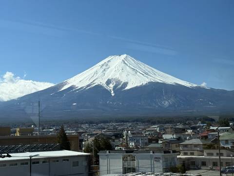       Snow-capped Mount Fuji dominates the horizon above a Japanese town under a clear blue sky.
  