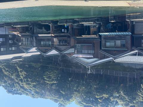       Traditional wooden boathouses line a teal-colored inlet beneath a forested hillside on a bright day.
  
