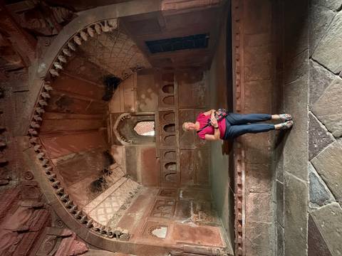       Traveller seated inside an ancient red-sandstone chamber with vaulted decorative ceiling and arched niches.
  