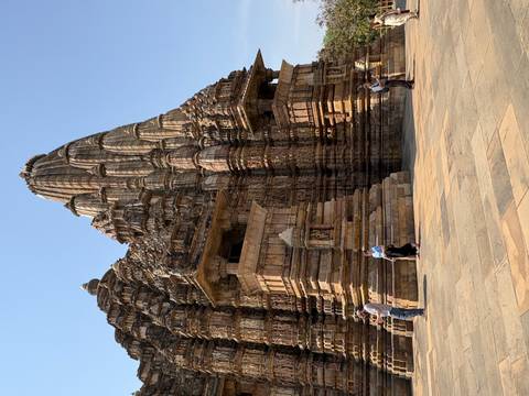       Elaborately carved sandstone temple tower of Khajuraho with tourists exploring the spacious courtyard.
  