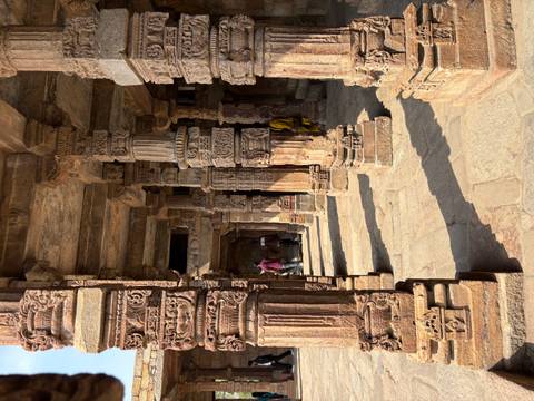       Stone pillars covered in ornate Hindu carvings illuminated by warm sunlight at an ancient temple.
  