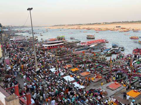       Panoramic view over Varanasi ghats showing crowds, ritual platforms and colorful boats on the Ganges River.
  