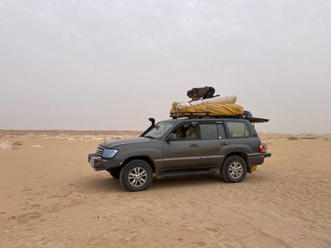       4x4 vehicle loaded with camping gear parked on vast sandy desert under hazy sky.
  