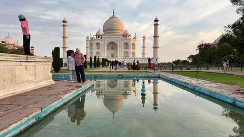       Visitors pose beside the reflecting pool with the Taj Mahal glowing in late afternoon light.
  