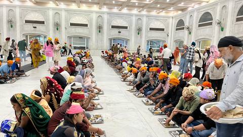       Long rows of pilgrims seated on the marble floor sharing a communal meal in a Sikh langar hall.
  