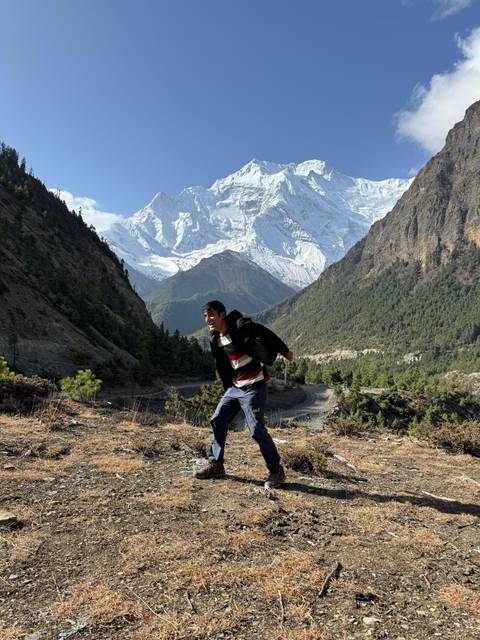       Young man posing energetically on hillside with snow-covered Annapurna range in background.
  