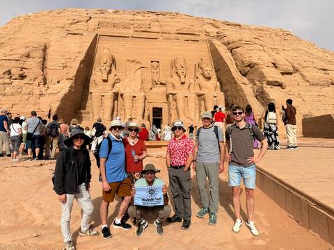      Tour group poses with banner in front of the colossal statues of Abu Simbel temple.
  