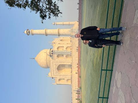       Couple stands arm in arm beside the Taj Mahal bathed in soft morning light.
  