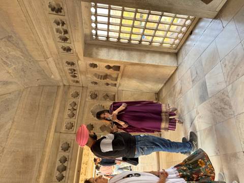       Man shows phone to woman dressed in traditional attire inside ornate marble chamber.
  