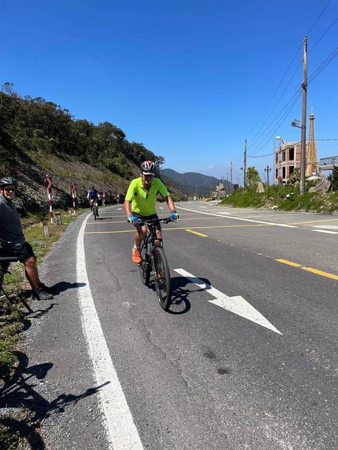       Cyclists riding along a mountain highway with a clear blue sky and rolling hills in the background.
  