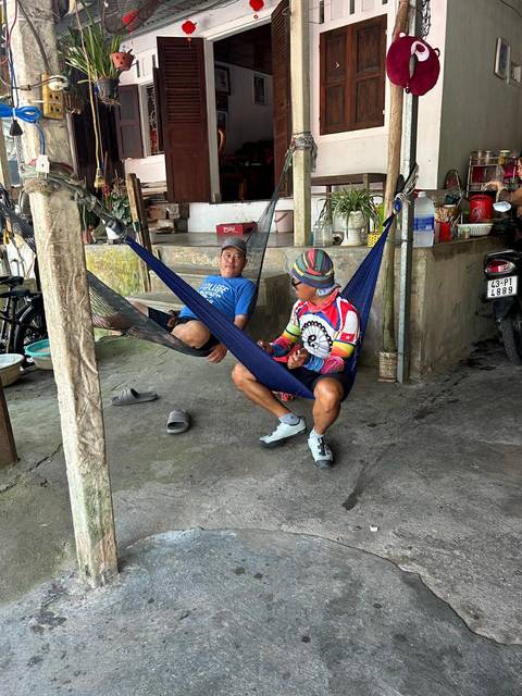       Two cyclists relaxing in hammocks at a rustic roadside rest stop.
  