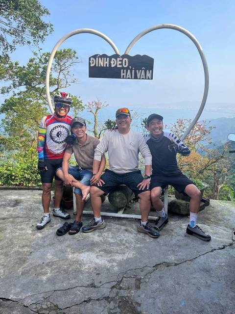       Four men posing at a scenic lookout with lush hills and distant bay behind them.
  