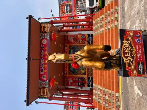       Golden horse statue with red bow in front of ornate Jonker Walk stage in Melaka.
  