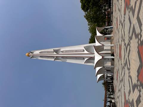       Tall white modern minaret-style tower rising against a clear blue sky in Melaka.
  