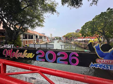       Colorful sign 'Visit Melaka 2026' spanning a pedestrian bridge over the Melaka River.
  