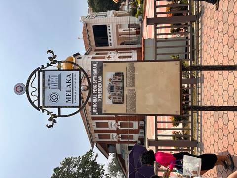       Informational heritage plaque in front of colonial building at Independence Memorial Melaka.
  