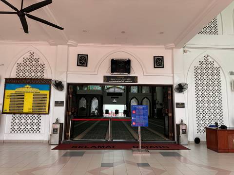       Entrance of a mosque with welcome sign and prayer rugs visible inside.
  