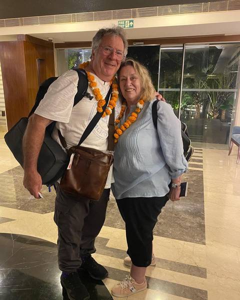       Smiling couple wearing marigold garlands arriving at an Indian hotel lobby.
  