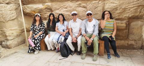      Small tour group resting on wooden benches against a sandstone wall inside an ancient Egyptian site.
  