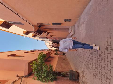       Young woman smiling while standing in a narrow terracotta-colored alleyway lined with Moroccan houses.
  