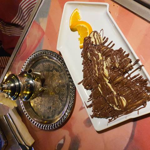       Plate of banana and chocolate crepe drizzled with rich sauce beside a traditional Moroccan tea set.
  