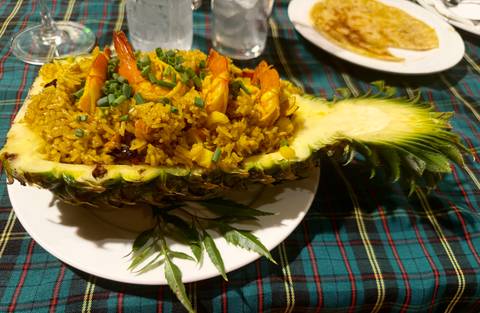       Thai pineapple fried rice served in a hollowed-out pineapple on a white plate over a plaid tablecloth.
  