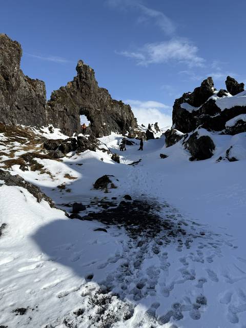       Snow-covered lava field with natural rock arch; hikers explore the icy volcanic landscape.
  
