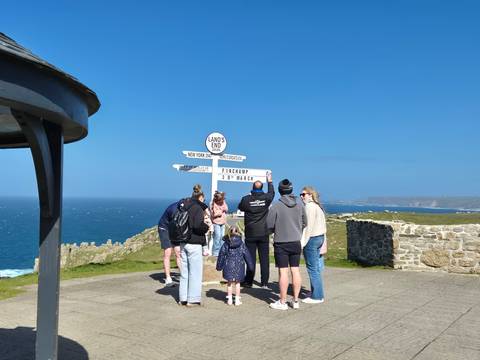       Visitors gather around the iconic white Land’s End signpost overlooking a rugged Atlantic coastline.
  