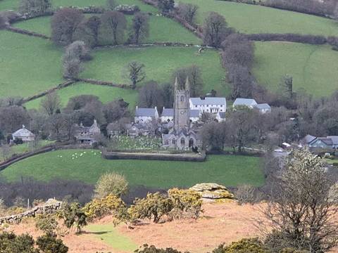       Distant view of a small English village with stone church and fields framed by rolling green hills.
  
