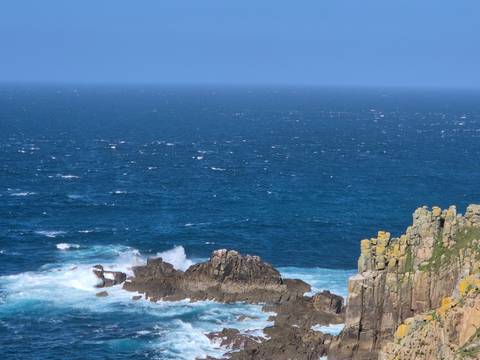      Blue Atlantic waves crash against rugged yellow-lichen covered cliffs.
  