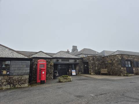       Stone courtyard with traditional slate-roof buildings and a classic red British phone box on a gloomy day.
  